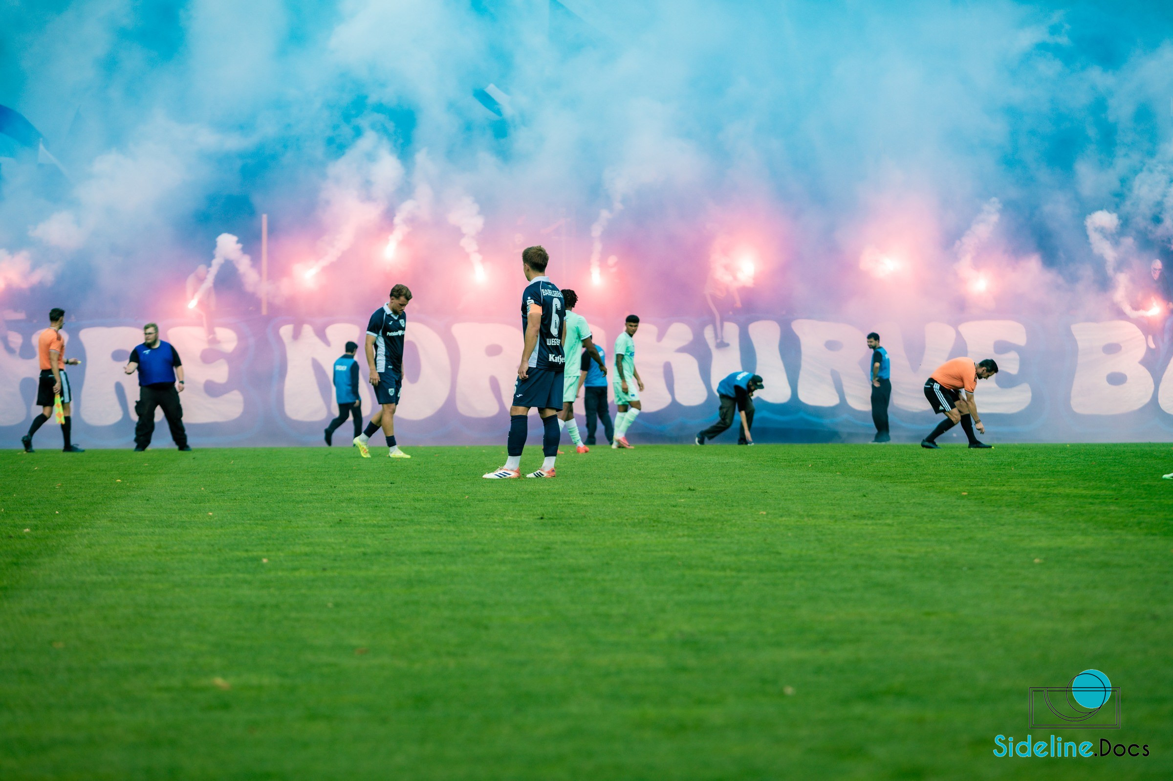 Players and officials in front of dense smoke and flares