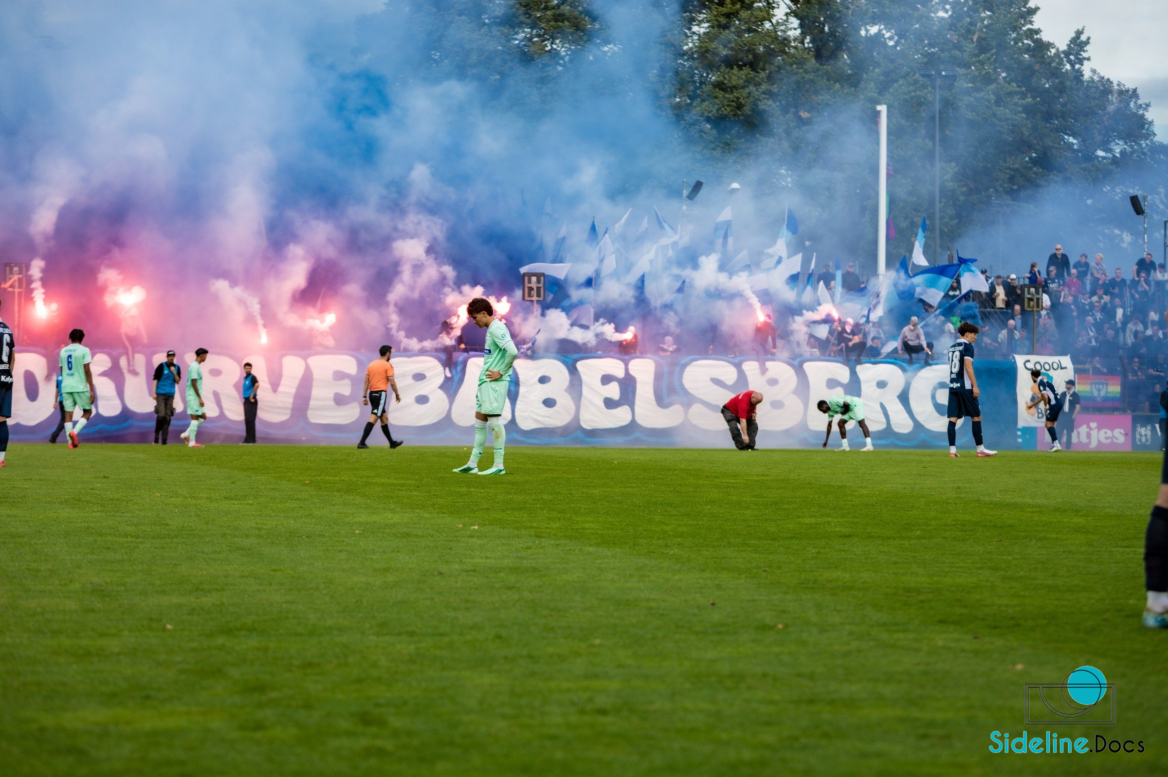 Hertha player in front of fading pyrotechnics and flags
