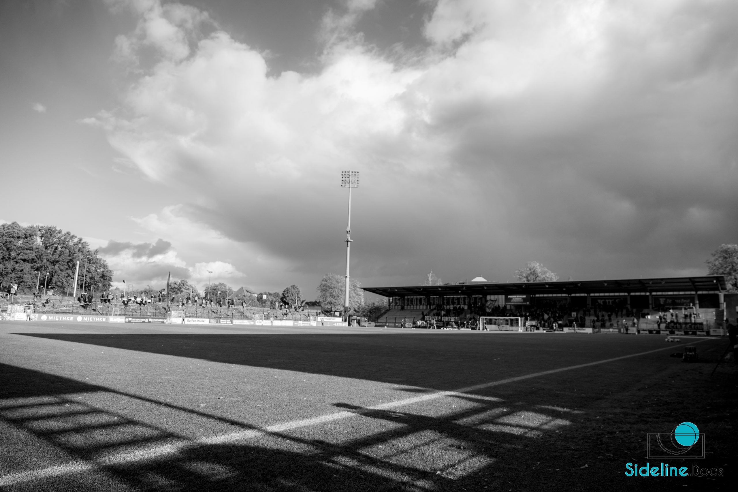 Wide view of the Karl-Liebknecht-Stadion under a heavy sky, shadows across the pitch