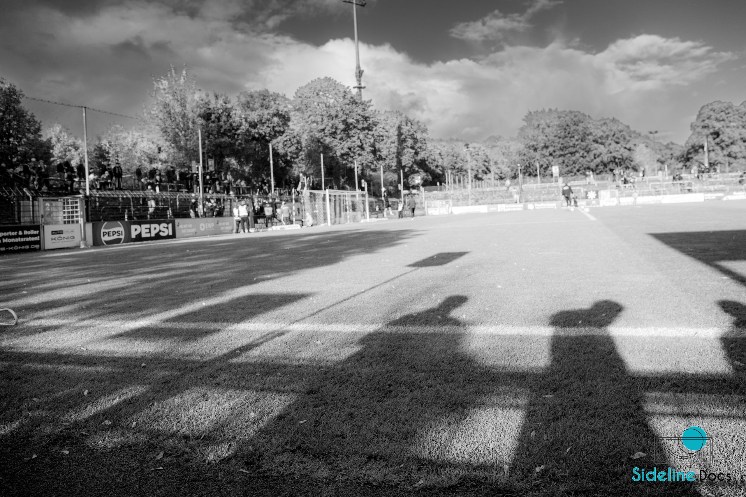 Long sideline shadows on the grass, advertising boards and the stand beyond