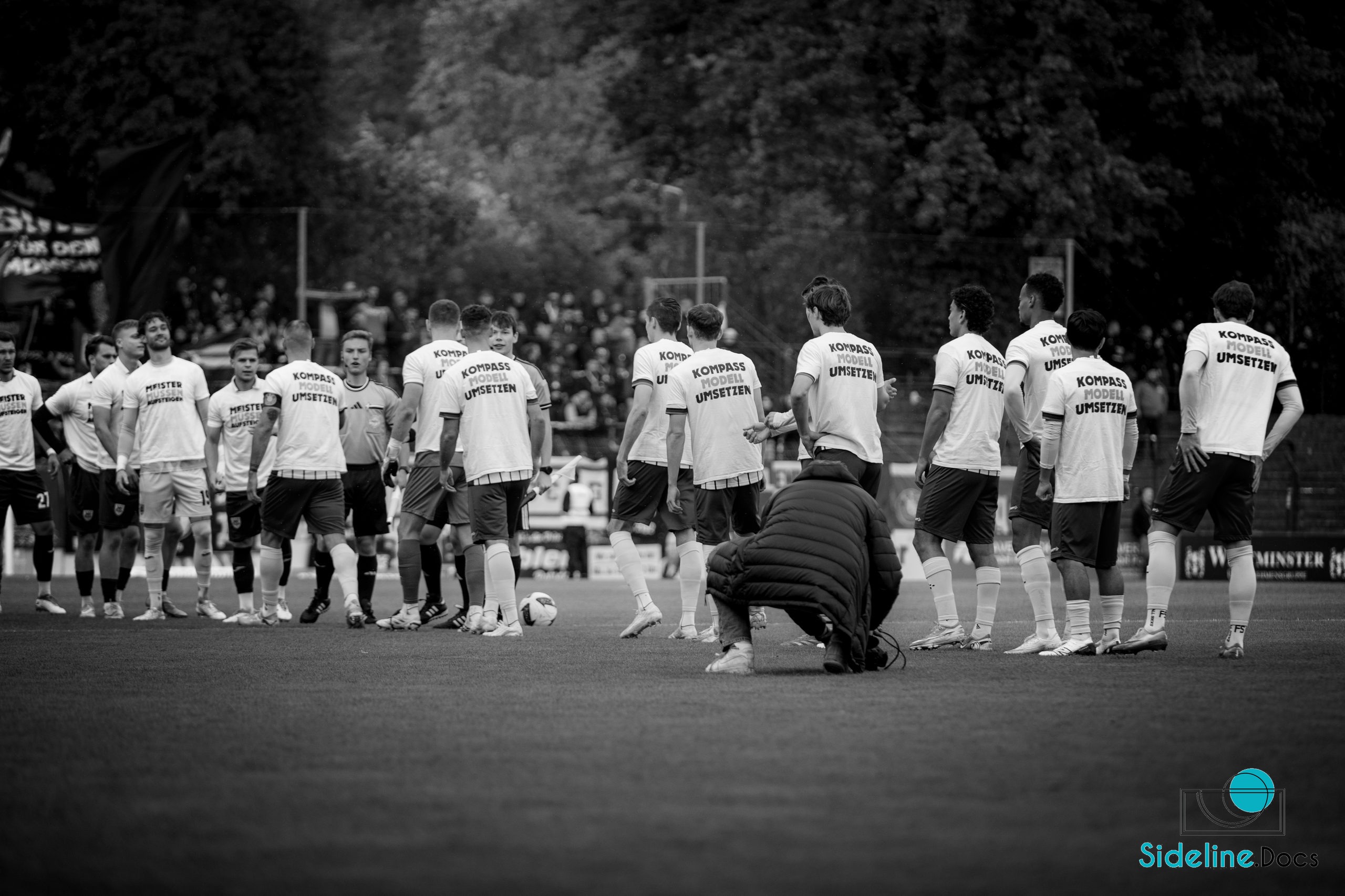 Players in white shirts reading KOMPASS MODELL UMSETZEN on the pitch