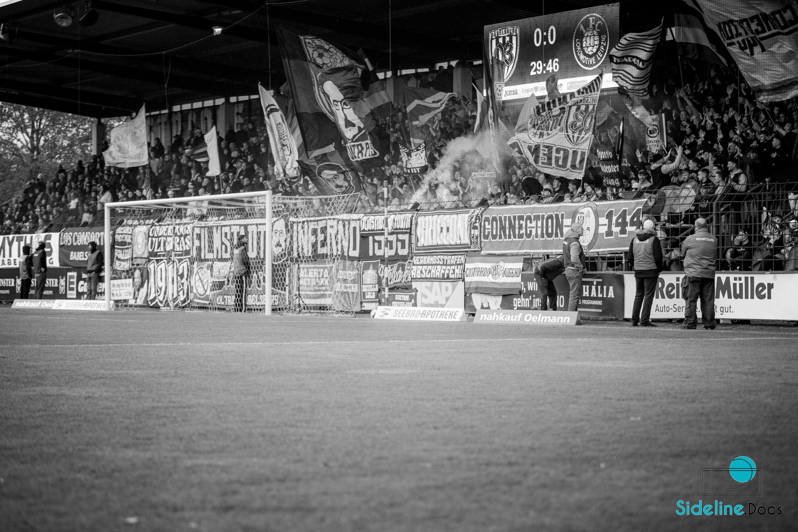 Home stand at 0–0, flags and smoke behind the goal