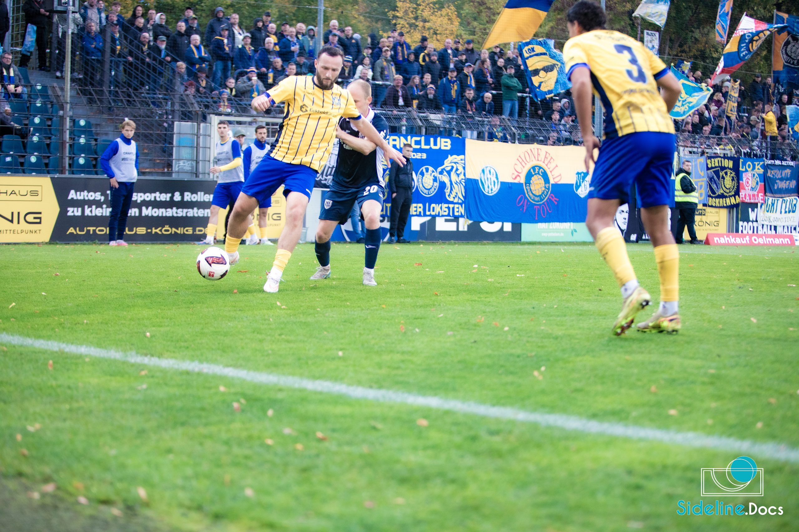 Lok Leipzig player in yellow-and-blue dribbles under pressure near the touchline