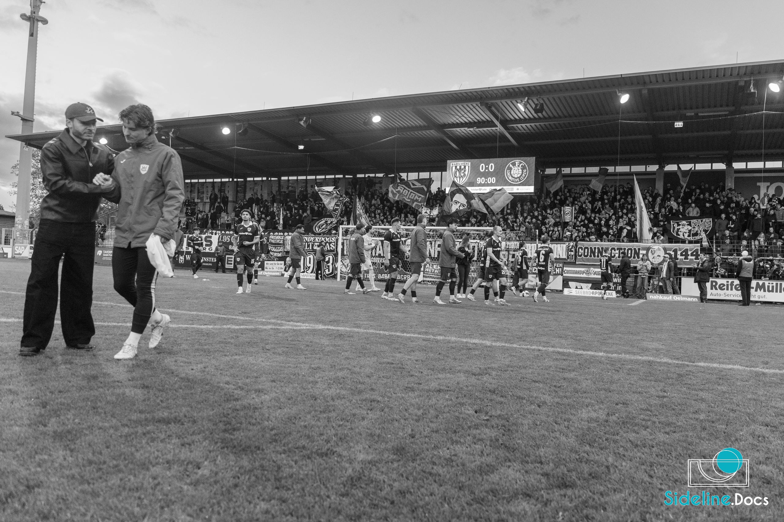 Two men leaving the pitch after full time, scoreboard at 0–0